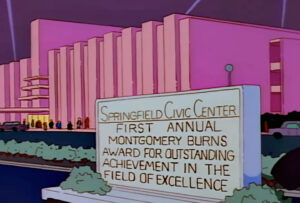 Screenshot from The Simpsons (s03e24, 'Brother, Can You Spare Two Dimes?') depicting a large pink Art-Deco-ish building, the Springfield Civic Center, with a sign outside annoucing the 'FIRST ANNUAL MONTGOMERY BURNS AWARD FOR OUTSTANDING ACHIEVEMENT IN THE FIELD OF EXCELLENCE'