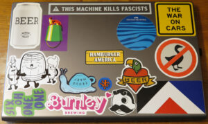 Stickers on the back of my laptop, including the one-eyed Mr Boh logo, the Red Peak flag, a Golding's Free Dive bucketlamp, The War On Cars podcast, Garage Project BEER and others