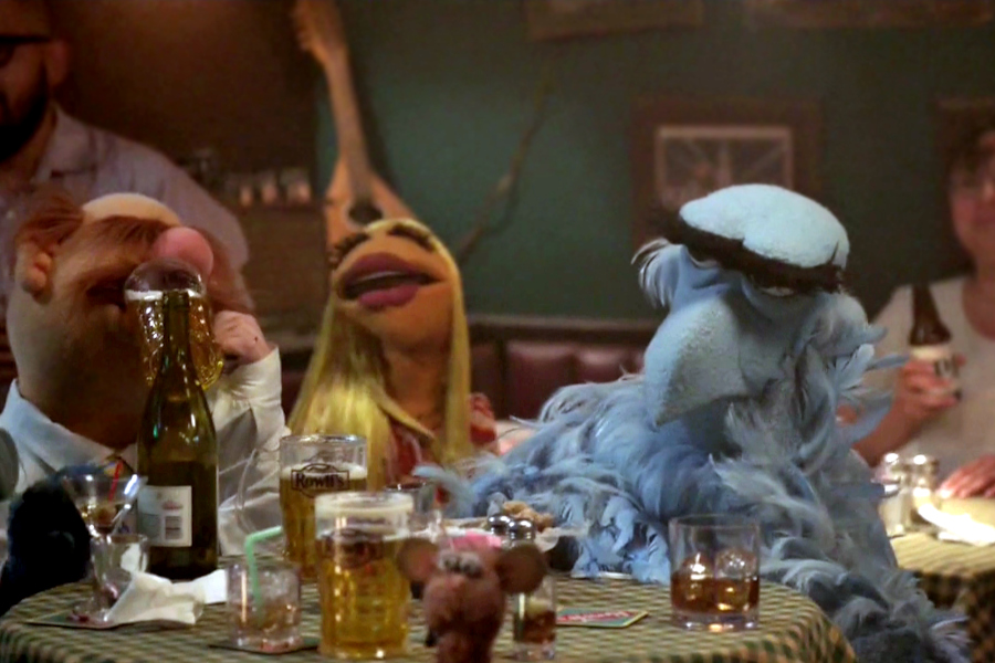 Screenshot from The Muppets (2015) episode 4. Swedish Chef, Janice and an exasperated Sam the Eagle are sitting at a table in Rowlf's Tavern
